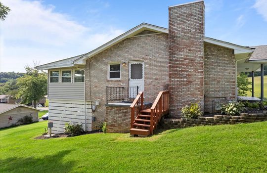 side view of home, brick exterior, landscaping, side porch, side entry door, sunroom, patio with privacy screen, yard, neighboring homes