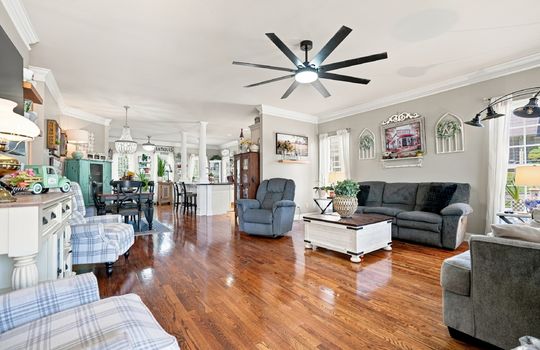 Living room, open floorplan to dining space and kitchen, hardwood flooring, oversized ceiling fan, windows