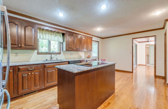 kitchen, hardwood flooring, exterior door, tile backsplash, granite countertops, cabinetry, cooktop, kitchen island, sink, window above sink, refrigerator, dishwasher