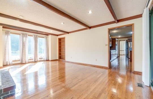 family room, fireplace, wood beam ceiling feature, recessed lighting, built-in shelving, windows, hardwood flooring, doorway to kitchen