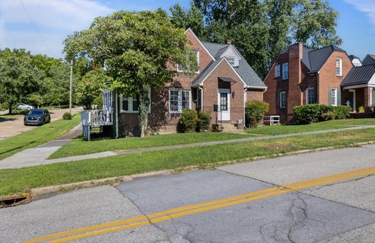 street view of home, tudor revival style home, brick exterior, shingle roof, side porch, landscaping, front yard, front stairs, sidewalk, neighboring home