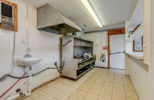 kitchen, tile flooring, sink, service/pass-through station, commercial vent hood, fluorescent lighting