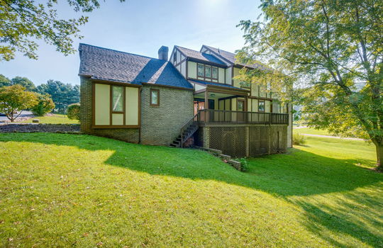 back of home, back yard, covered back deck, back porch, tudor style home, brick, wood siding, landscaping