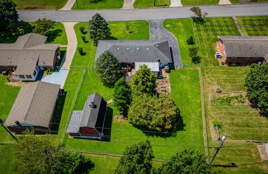 aerial view of home, back of home, storage shed/outbuilding, backyard, trees, landscaping, fenced back yard, shingle roof, driveway, front yard, road, neighboring homes