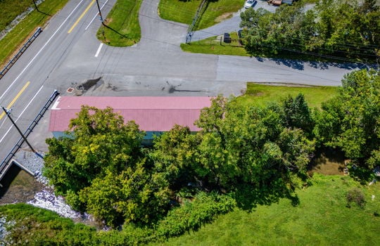 overhead aerial view of property, commercial space for lease, road, parking lot, parking spaces, metal roof, stone exterior, nearby properties, mountain views