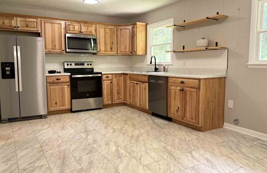 kitchen, eat in kitchen, cabinets, countertops, tile backsplash, painted paneling, stainless steel appliances, refrigerator, range/oven, built in microwave, sink, window above sink, dishwasher, shelving