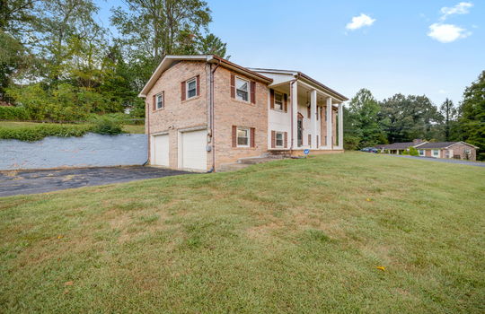 left side view of home, front yard, split level home, brick, covered front porch, front door, driveway, two car garage, drive under garage