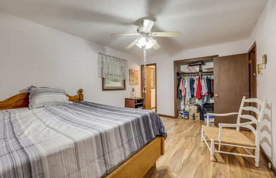 primary bedroom, closet, wood trim, door to half bath, hardwood flooring, ceiling fan, window