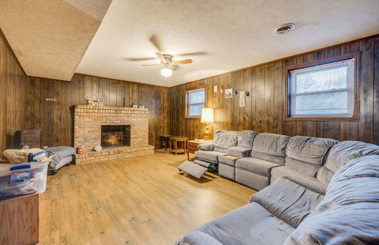 lower level den, windows, paneling walls, brick fireplace, ceiling fan, hardwood flooring