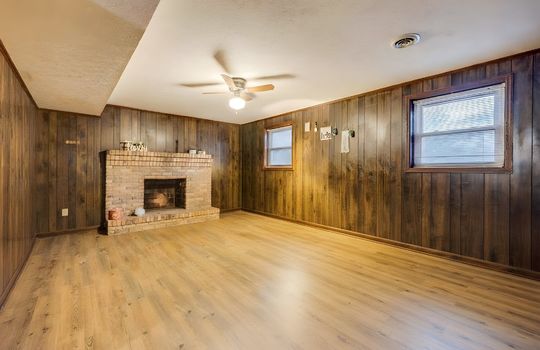 lower level den, paneling walls, ceiling fan, hardwood flooring, digitally altered to remove furniture, brick fireplace, windows