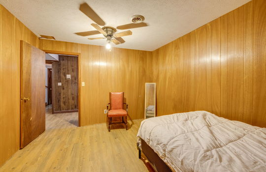 lower level bedroom, ceiling fan, paneling walls, hardwood flooring