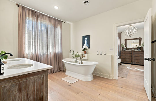 main level primary bathroom, double vanity sink, bathtub, windows, hardwood flooring