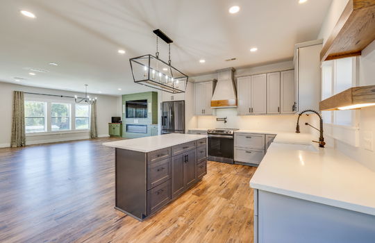 kitchen, kitchen island, refrigerator, oven/range, countertops, cabinets, sink, apron sink, luxury vinyl flooring, view toward living room, fireplace, windows