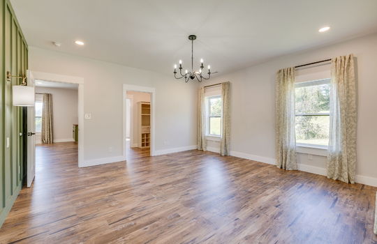 bedroom, view into living room, board and batten feature wall, sconces, chandelier, windows, luxury vinyl flooring, view into walk-in closet/primary bath