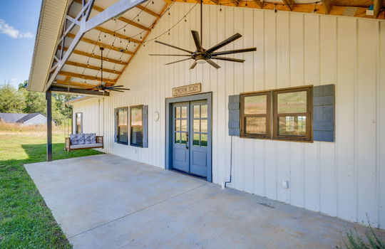covered porch, metal siding, large outdoor ceiling fan, porch swing, entry door, windows