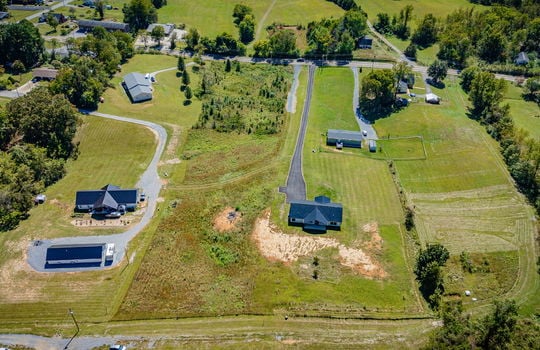 aerial view of home toward road, back of home, back yard, metal roof, driveway, neighboring homes, trees