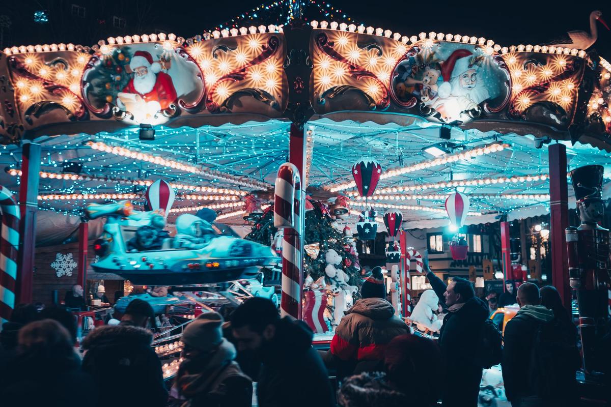 Lit-up holiday carousel with Santa panels and candy-cane poles at a night Christmas market