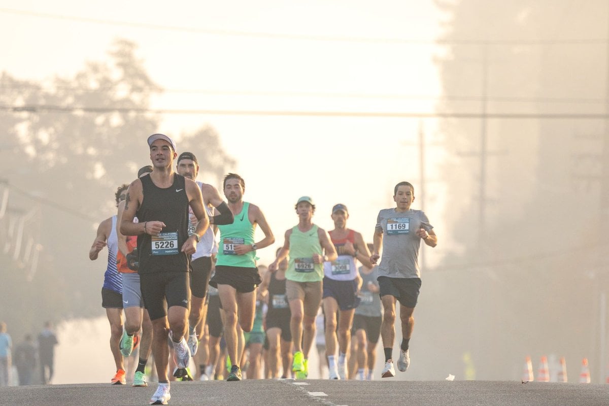 Runners wearing race bibs on a road during a hazy morning road race
