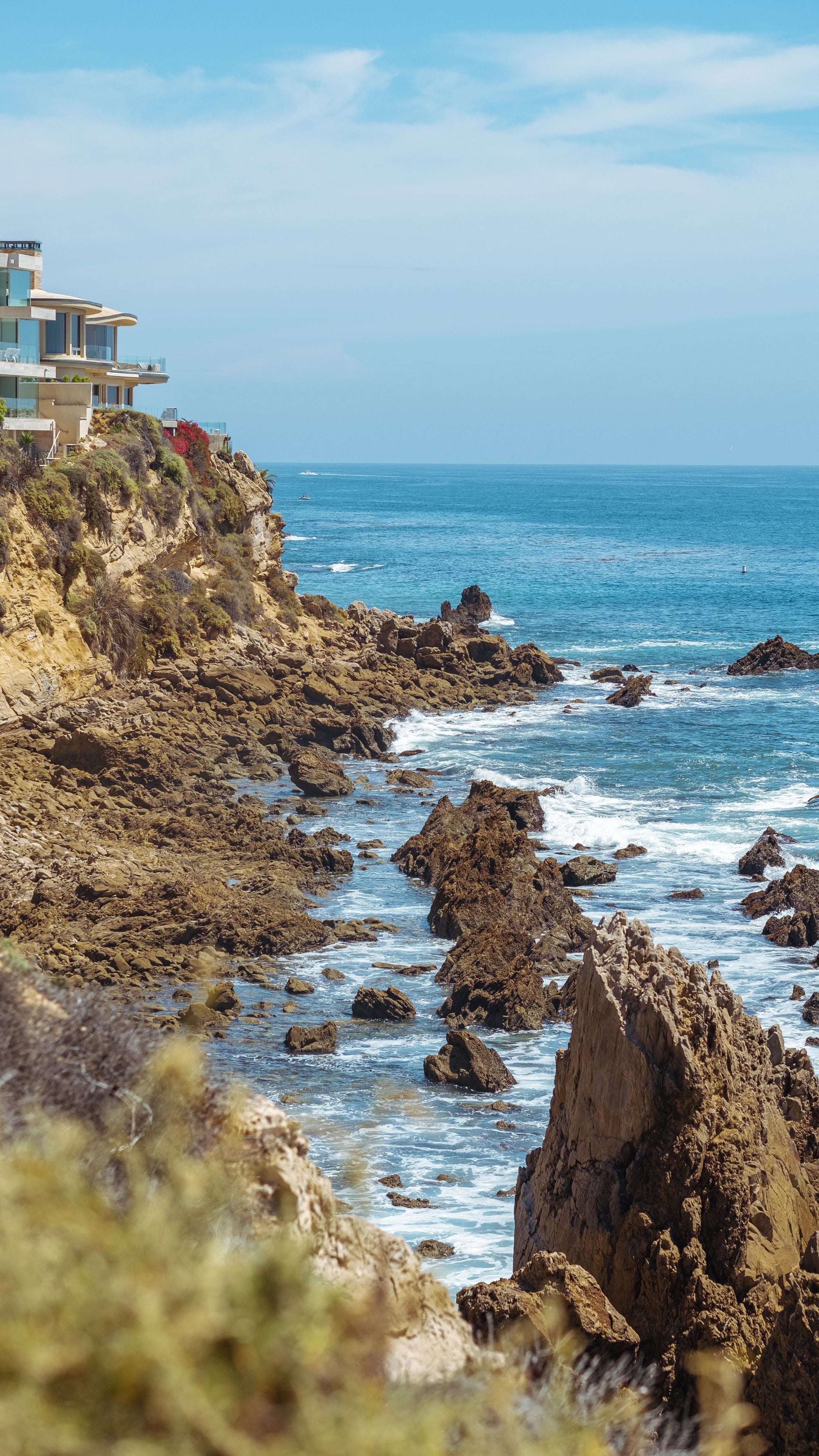 Waves breaking against a rocky Southern California coastline under a bright sky