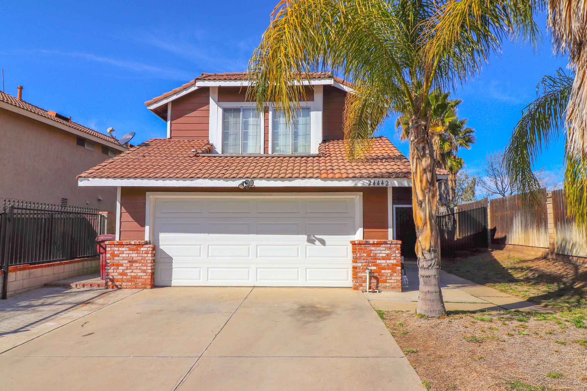 A sunlit suburban house with a garage and palm trees in the driveway