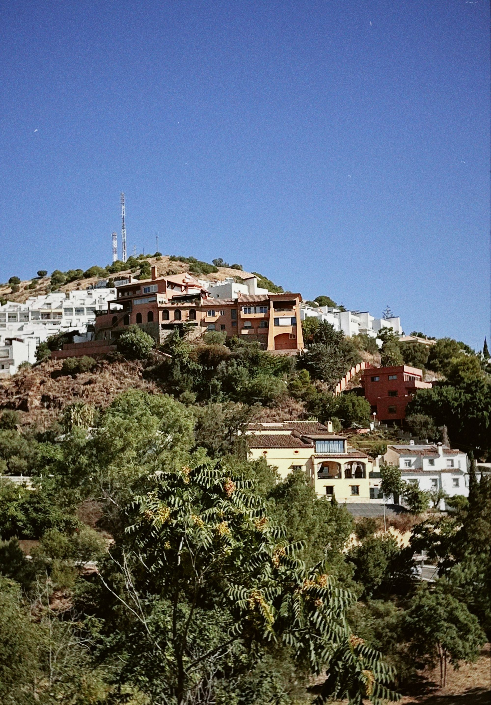Homes on a hilltop surrounded by greenery under a clear blue sky