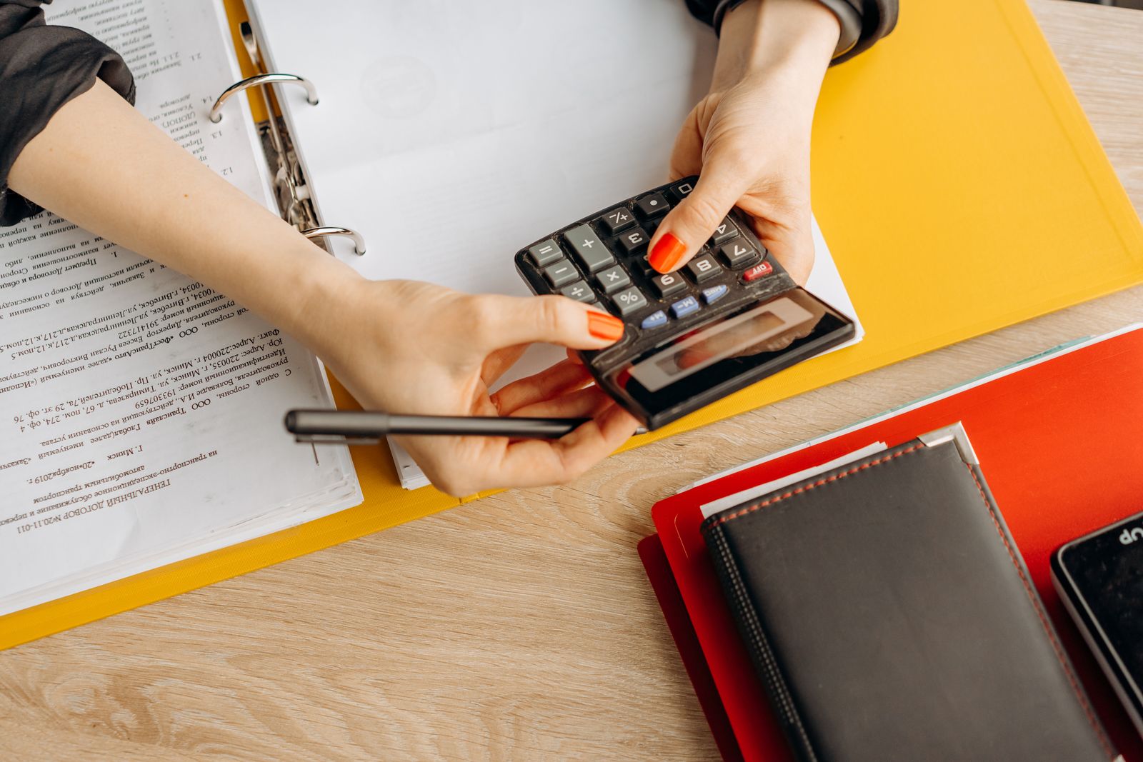 A pair of hands working a calculator at a desk covered with printed financial documents and folders