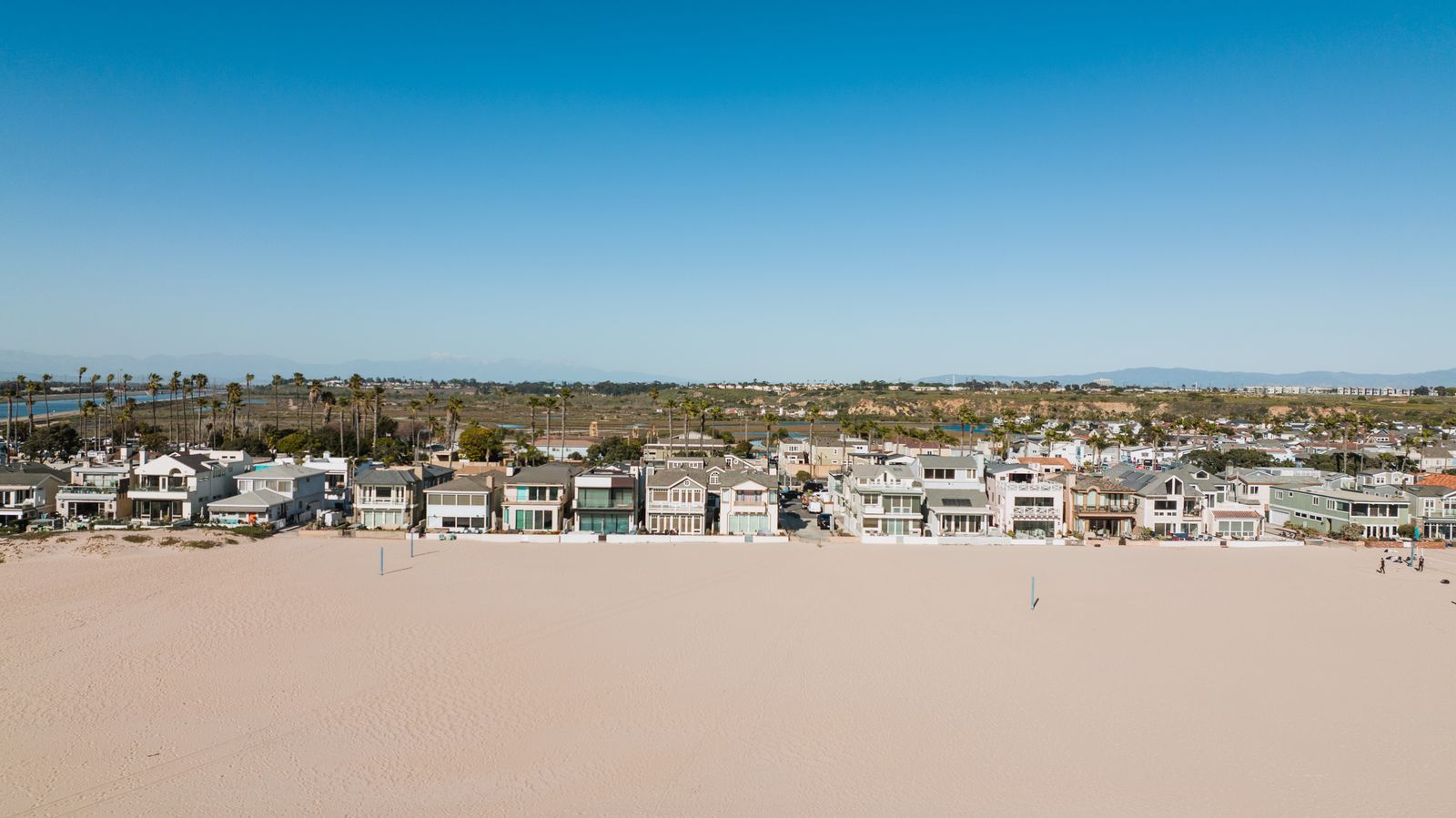 A row of oceanfront houses facing a wide stretch of empty sand under a clear sky.