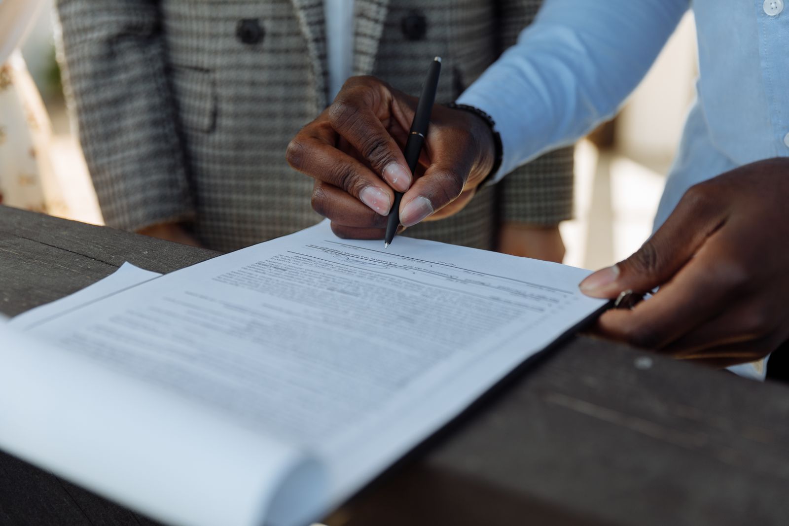 Two people at a desk signing a printed document with a pen during a professional meeting
