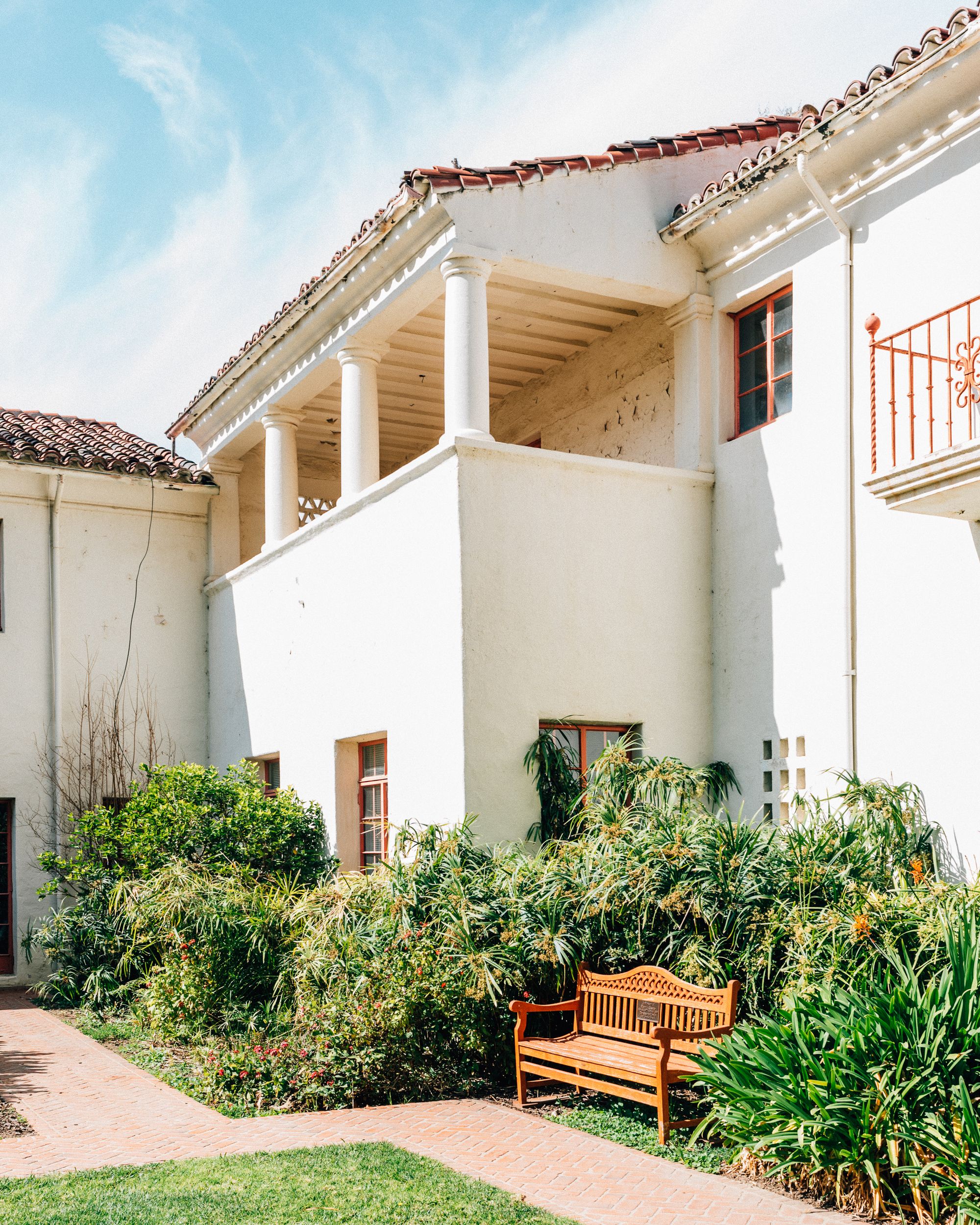 A low rise white stucco building with green foliage in bright sunlight