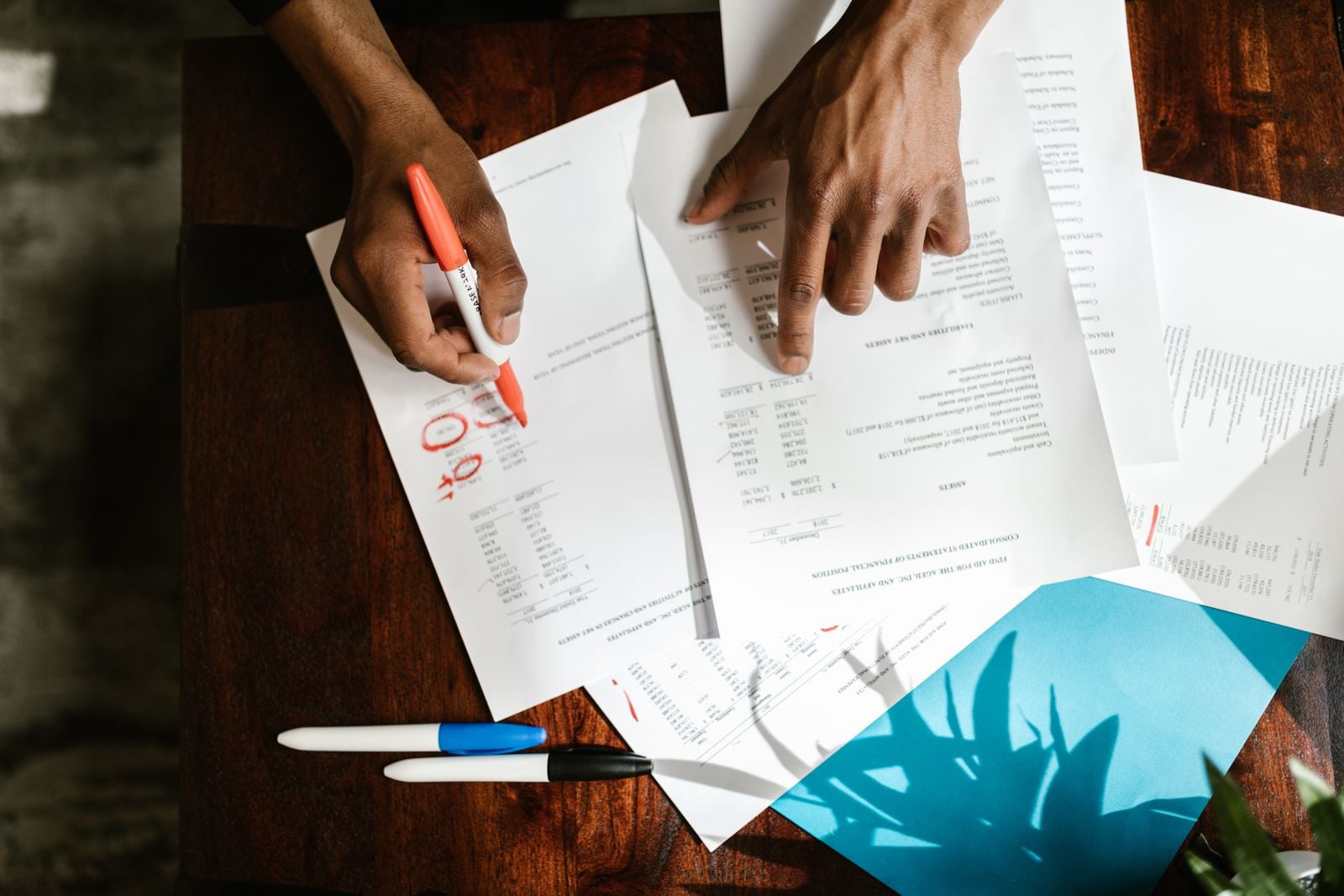 Overhead view of hands marking up a financial document on a desk with a pen