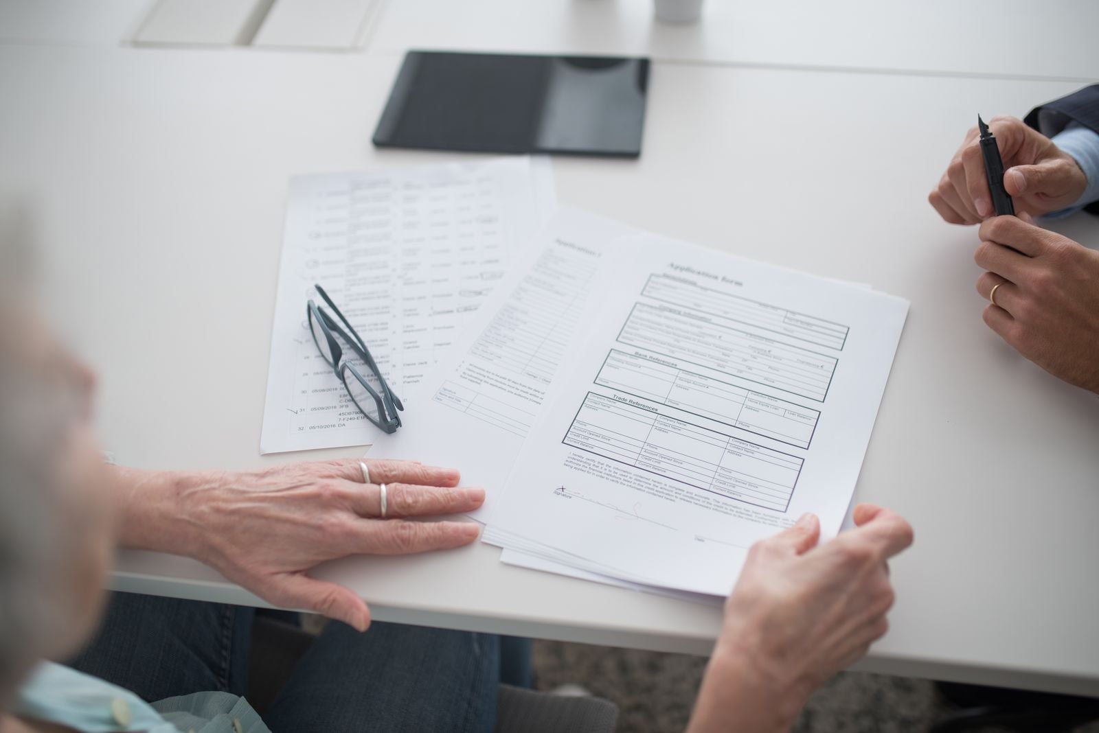 Two people seated at a table reviewing printed trust documents, with a pair of reading glasses resting on the pages