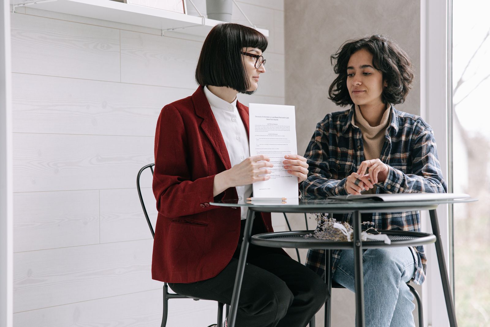 Two women seated indoors at a table, reviewing printed real estate documents together