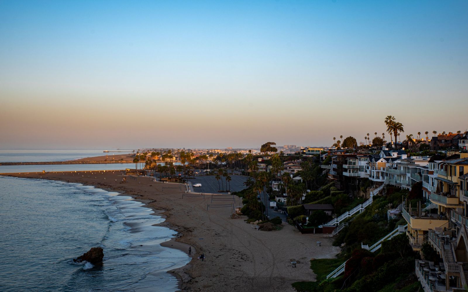 Aerial view of homes on a coastal hillside above a sandy beach at golden hour