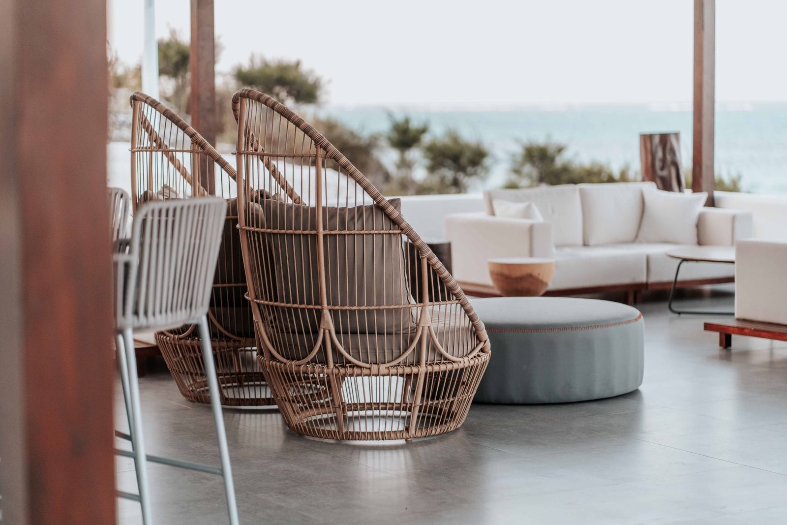 Wicker lounge chairs and a white sofa on a covered terrace facing the ocean