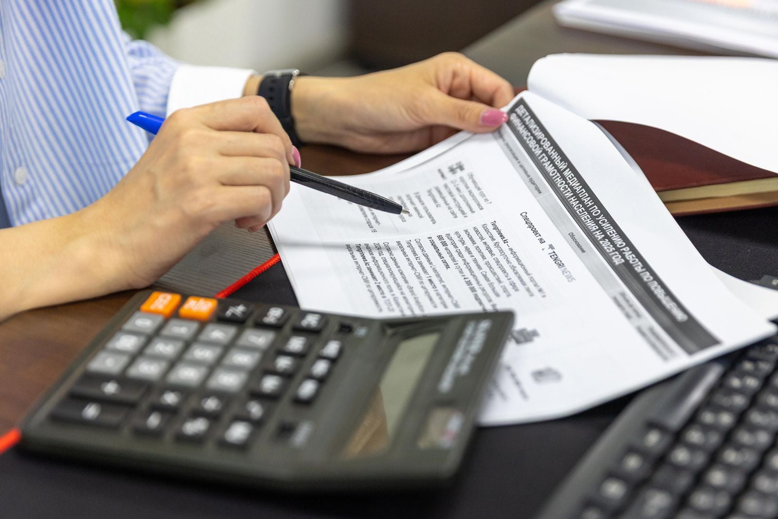 Close-up of a person reviewing printed financial documents with a calculator and a pen