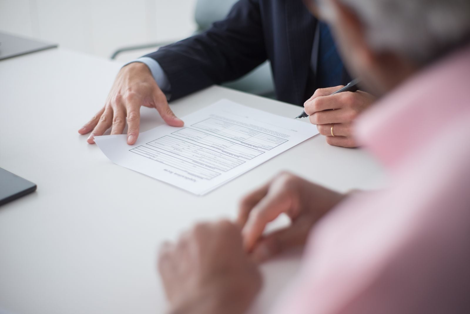 Two people reviewing a printed contract at a white conference table, one pointing at a clause while the other holds a pen