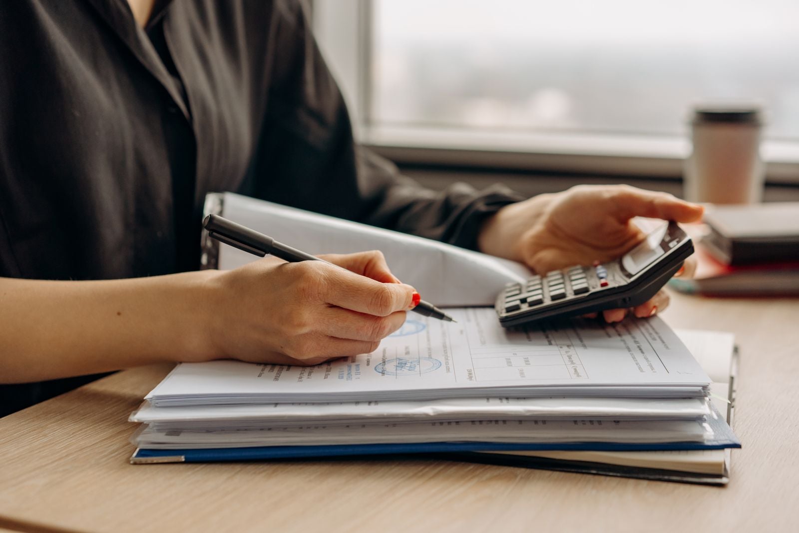 Person working through paperwork with a pen and a calculator at a desk