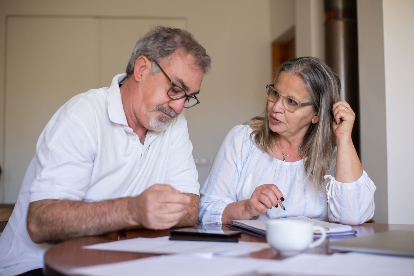 An older couple sitting at their dining table going over printed paperwork with a calculator between them