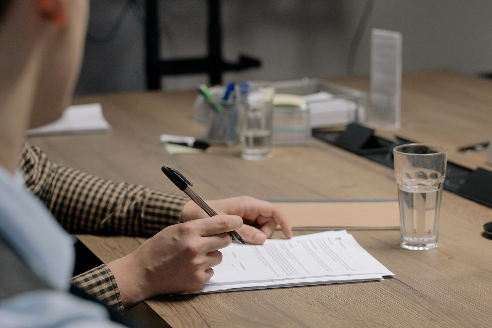 Person signing a stack of printed documents at a desk with a pen in hand