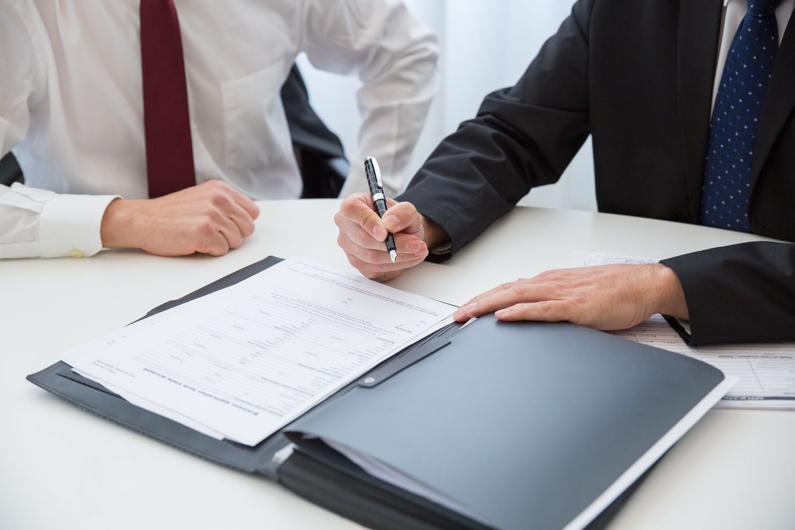 A person in a dark suit holding a pen above contract pages spread across a table