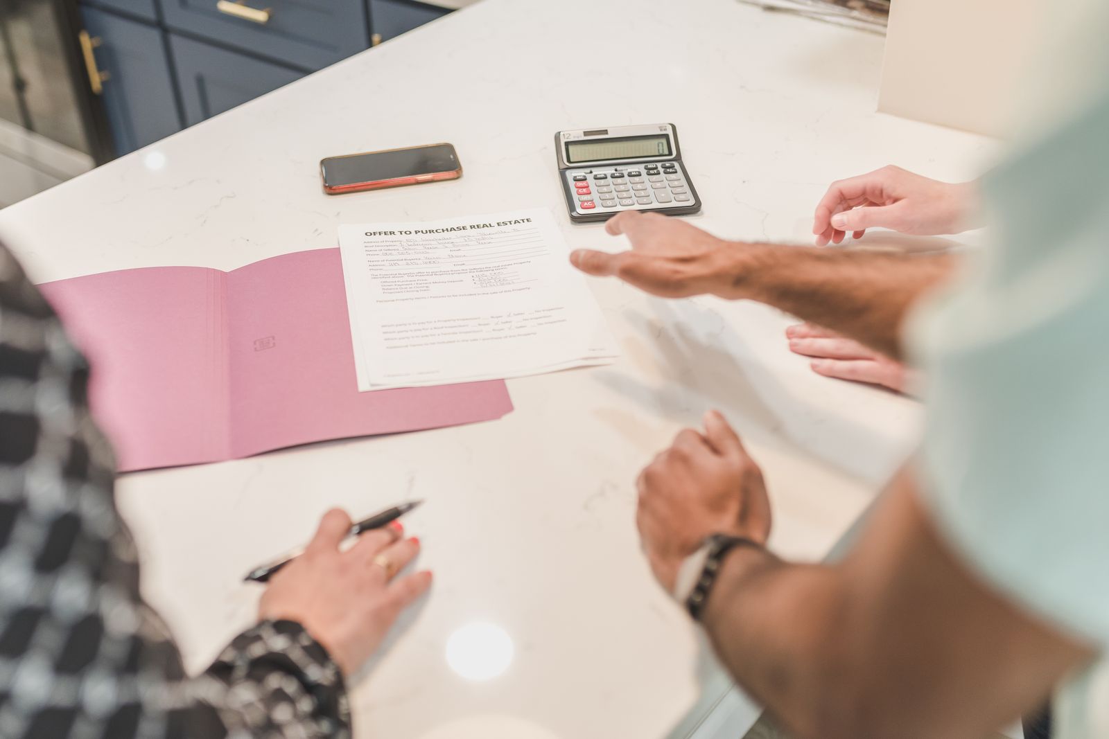 An offer to purchase real estate form on a table beside a calculator while two people point at it