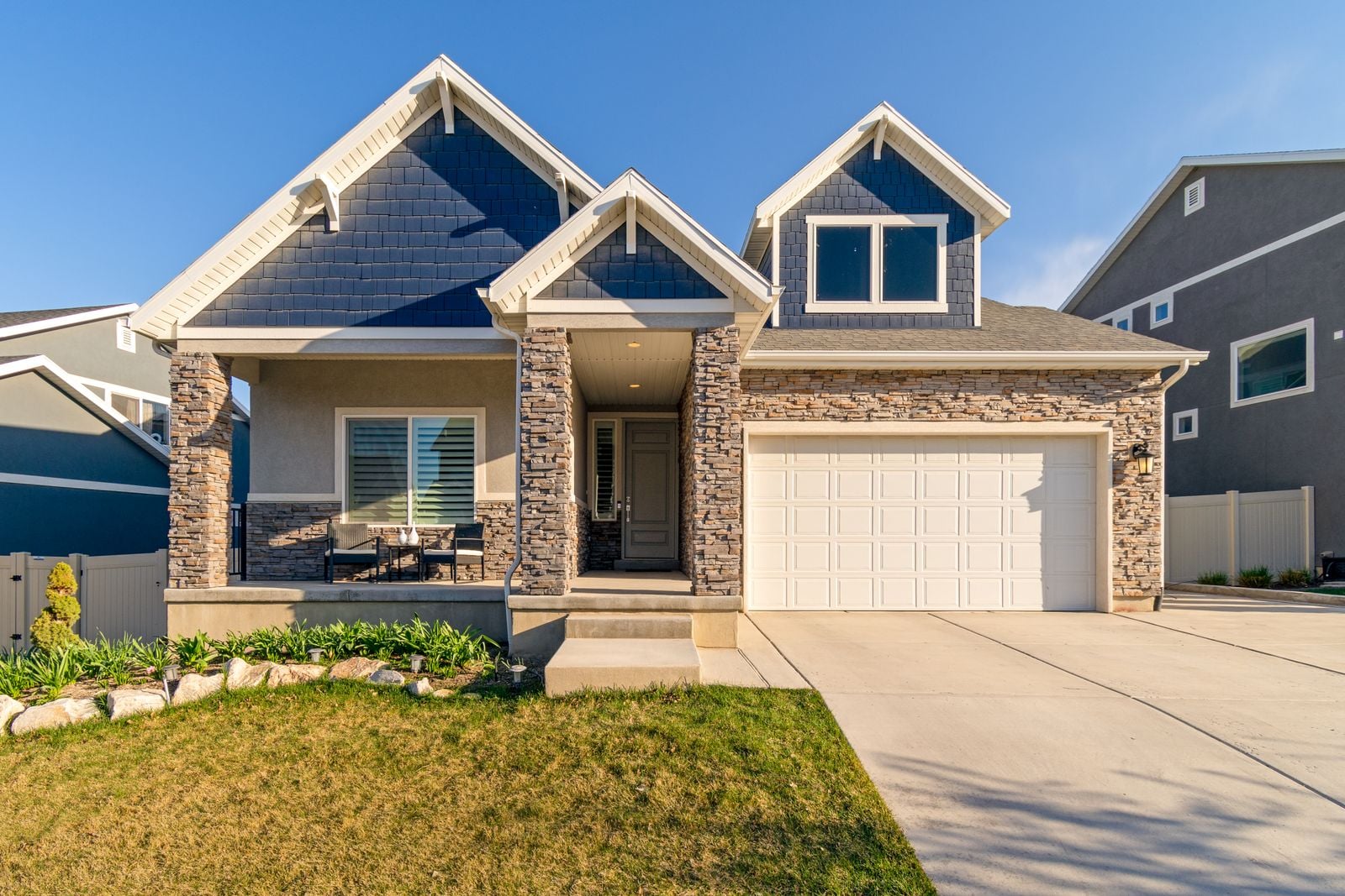 A two-story suburban house with a stone facade, attached garage and front lawn on a clear day
