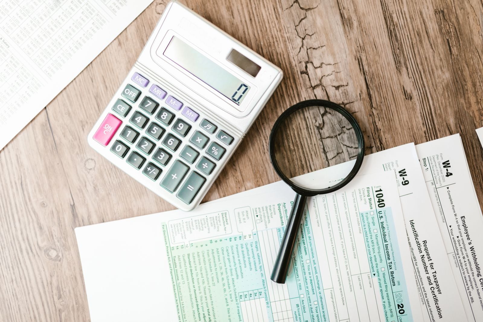 Federal tax forms spread on a wooden desk beside a calculator and a magnifying glass