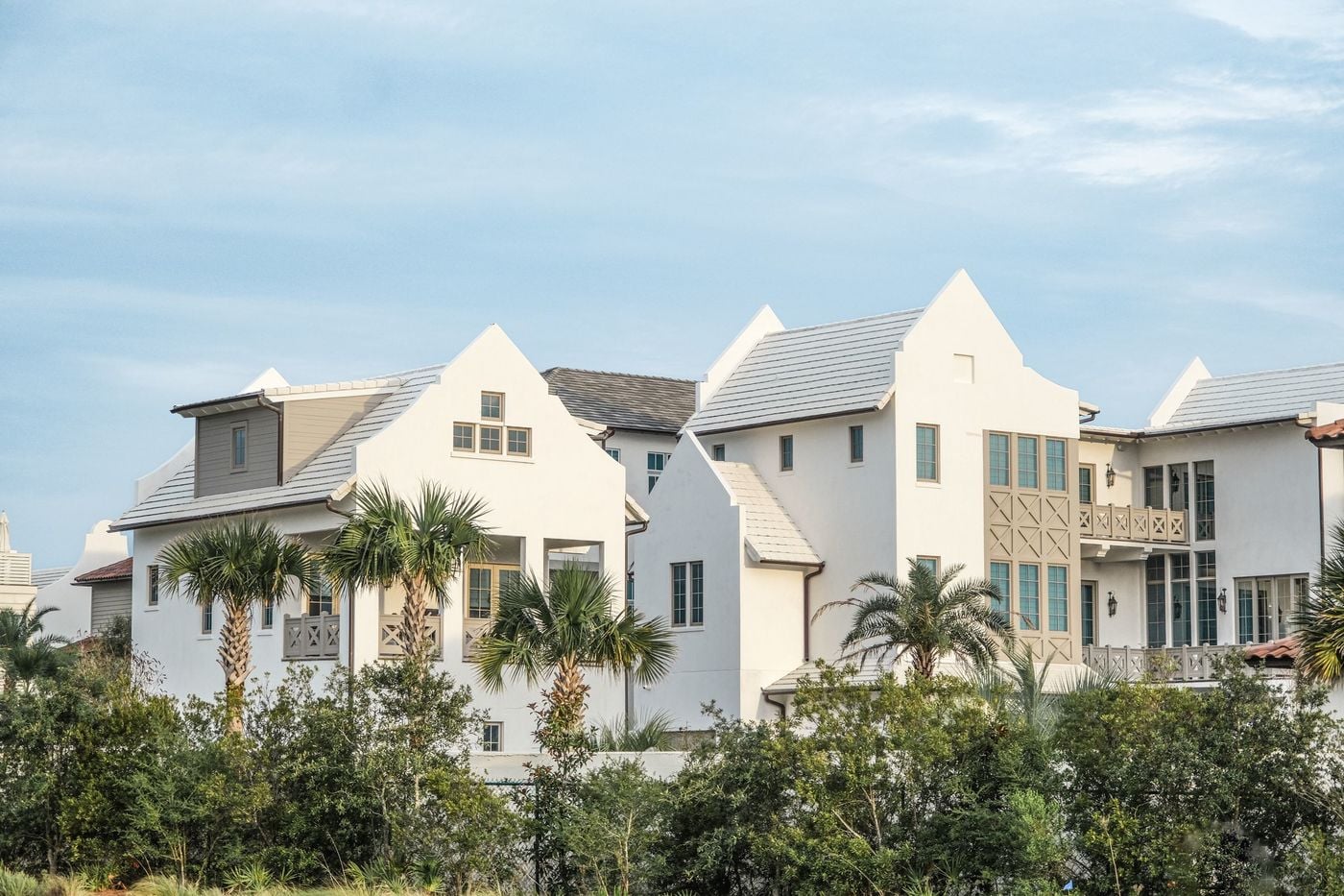 White coastal homes framed by palm trees under a soft sky