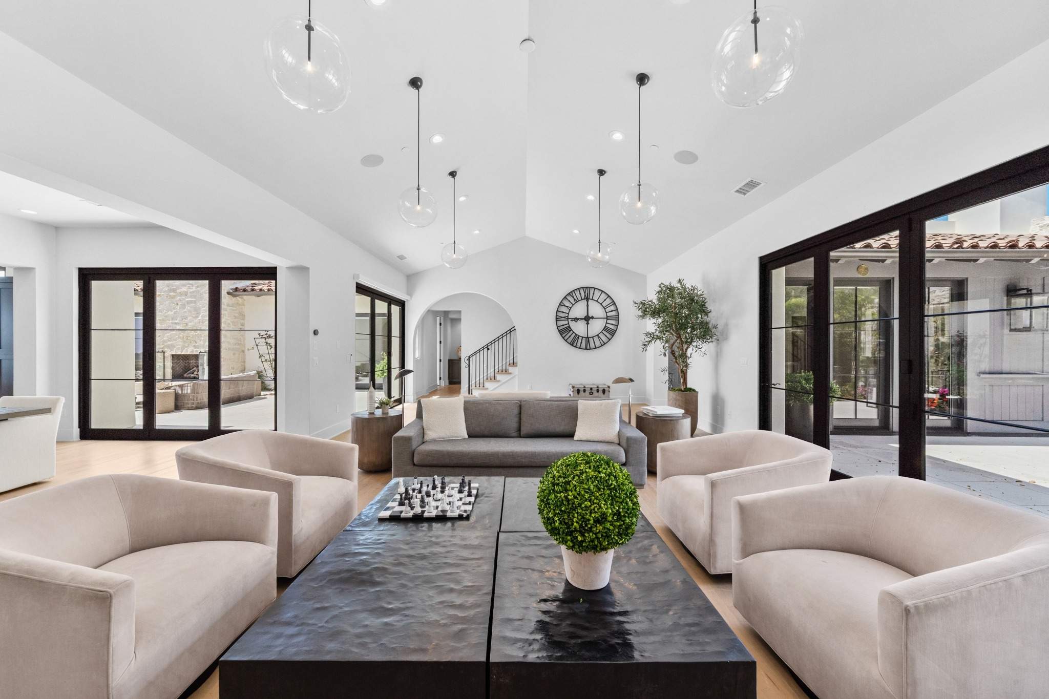 Spacious modern luxury living room with high ceilings, neutral seating, black coffee table, and large glass doors.