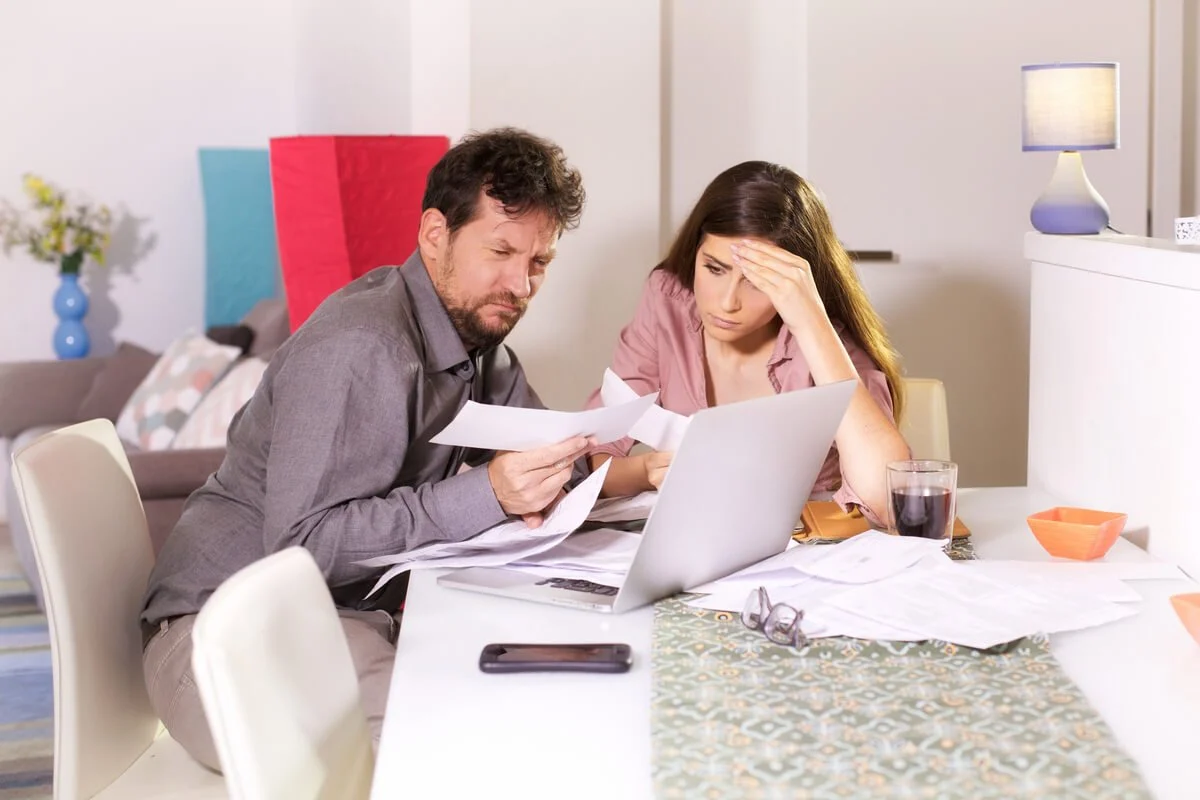 Couple stressed while reviewing second home expenses and mortgage paperwork at kitchen table