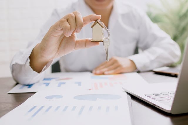 person holding up a house key at work desk covered in documents