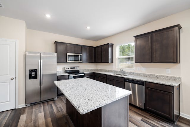 a beige kitchen with speckled granite counters and dark wood cabinets