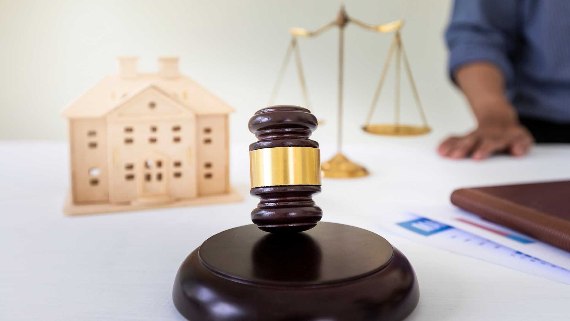 a gavel, legal balance and wooden home figurine on a desk