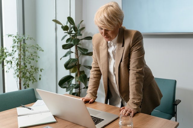 property manager in tan suit jacket leaning on desk looking at their computer